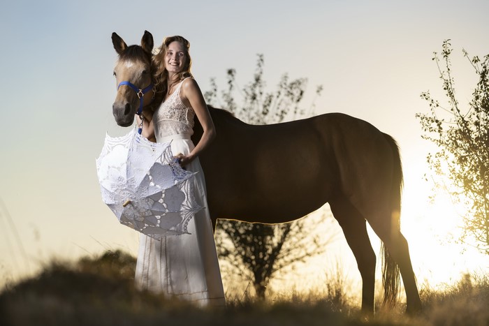 Woman with horse and umbrella at sunset
