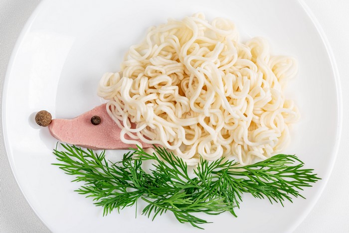 Hedgehog made of noodles, sausage, and dill on a plate