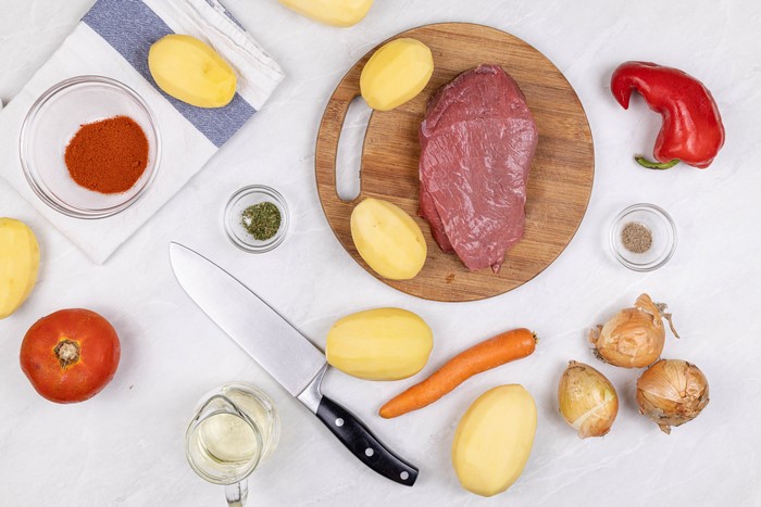 Raw Beef, Potatoes, Carrots, Onions, Bell Pepper, Tomato, Spices, Knife, Cutting Board