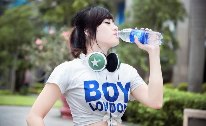 Girl drinking water with headphones and "BOY LONDON" shirt