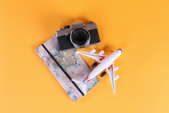 Camera, map, and airplane toy on orange background