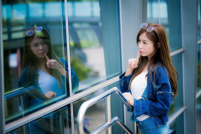 Asian woman with finger to lips in denim jacket
