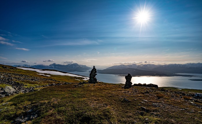 Two stone cairns on a grassy hill overlooking a fjord