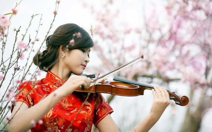 Asian woman in red dress playing violin with cherry blossoms