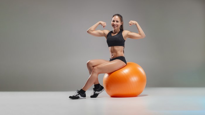 Fit woman flexing on an orange exercise ball