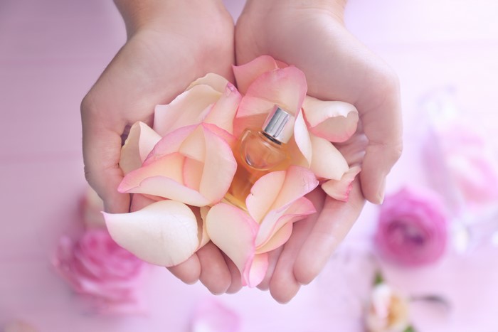 Hands holding rose petals and perfume bottle