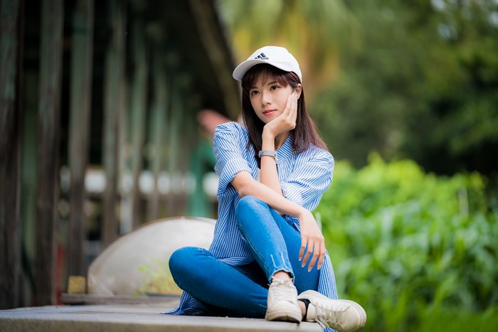Asian woman in jeans and baseball cap sitting outdoors