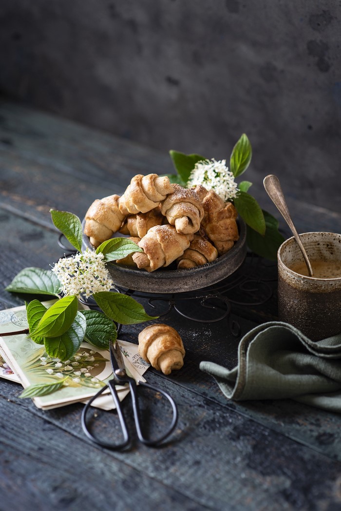 Croissants on a dark wooden table with flowers and scissors