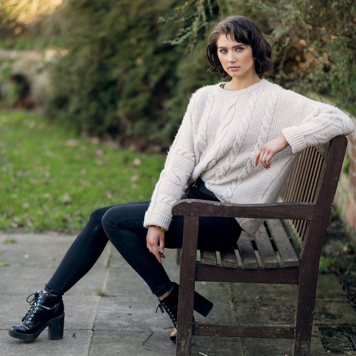 Abigail sitting on a bench wearing a sweater and jeans