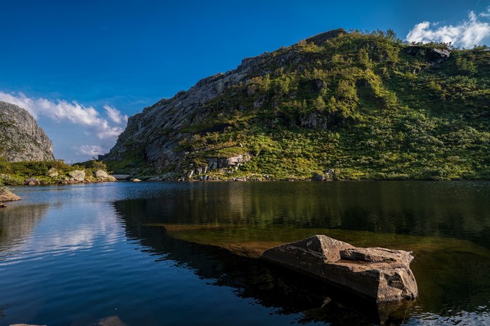 Mountain lake with rocky shore and green hills in Norway