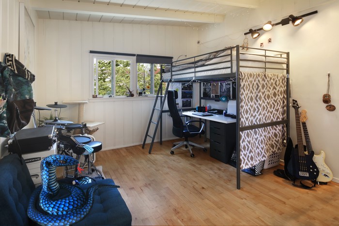 Loft bed with desk, drum set, and guitars in a room