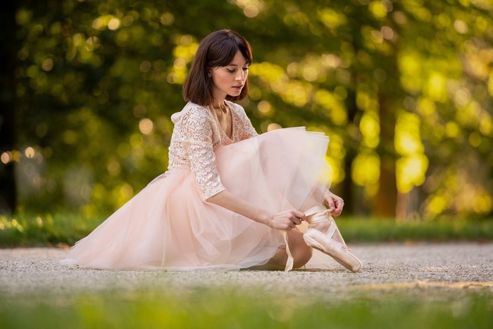Ballerina tying pointe shoes in park