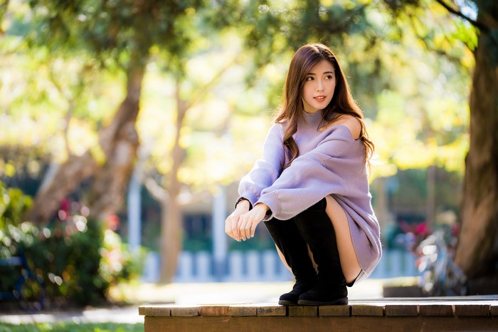 Asian woman in sweater sitting in park