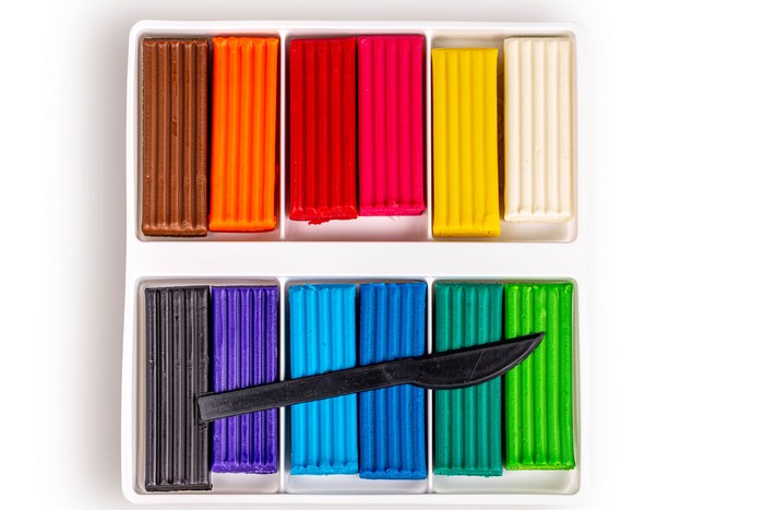 Multicolor plasticine sticks with a knife in a white tray