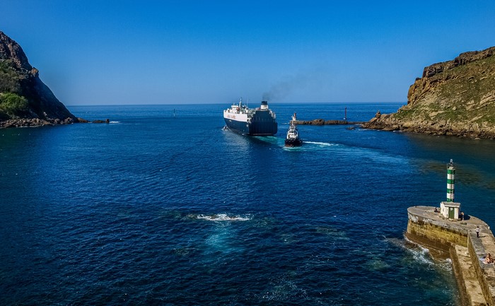 Ship and tugboat entering a bay with lighthouses in Spain
