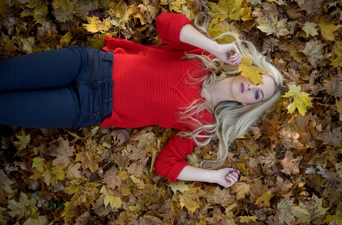 Blonde girl in red sweater lying in autumn foliage