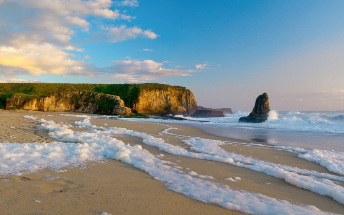 Ocean waves crash on a sandy beach with sea foam