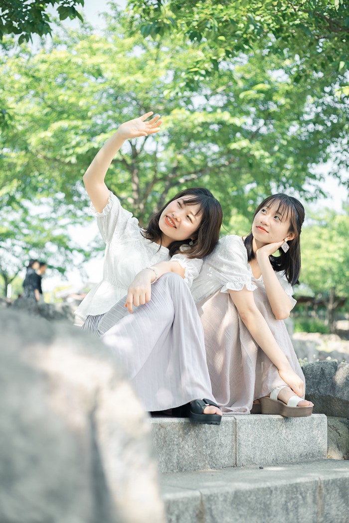 Two young Asian women sitting on stone steps outdoors