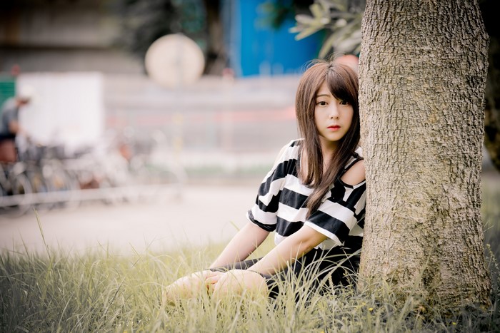 Asian girl with brown hair sitting by a tree