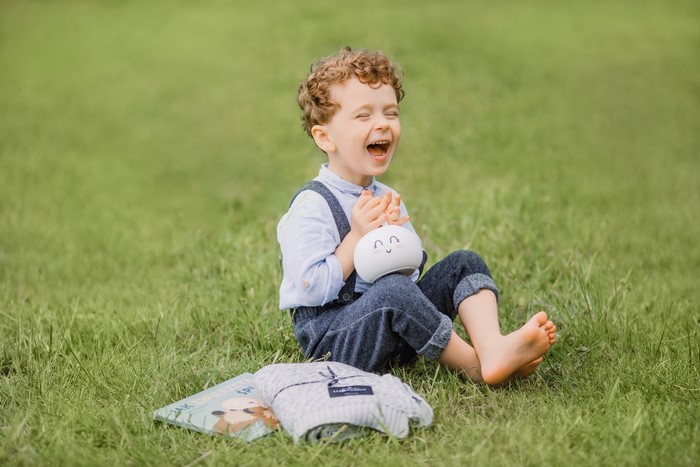 Boy laughing with a toy and books on grass