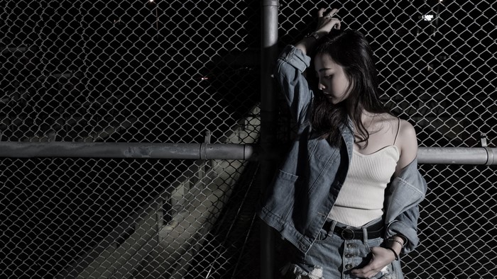 Brunette girl in denim jacket leaning on fence