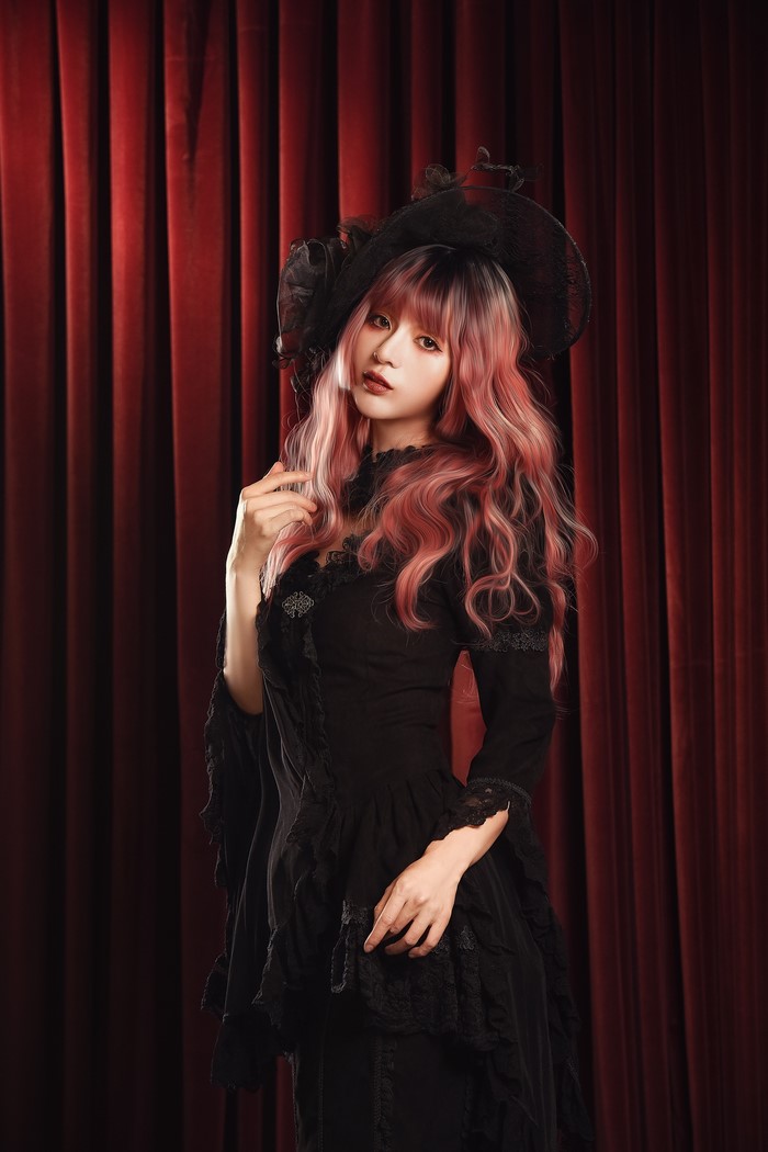 Asian woman with pink hair wearing a black dress and hat