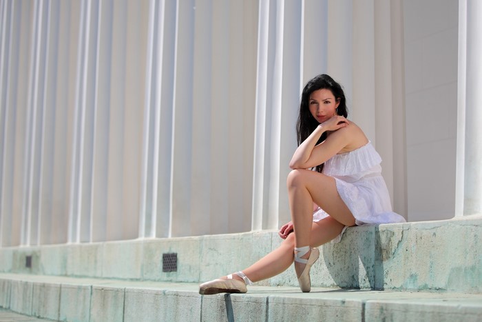 Brunette girl in white dress sitting by columns