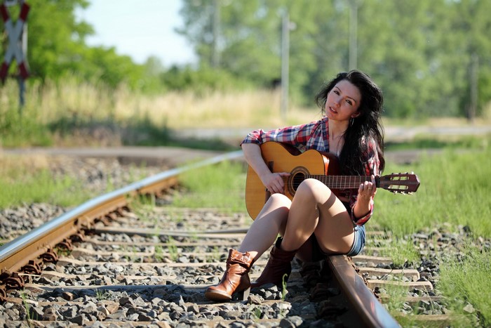 Brunette girl with guitar sitting on train tracks
