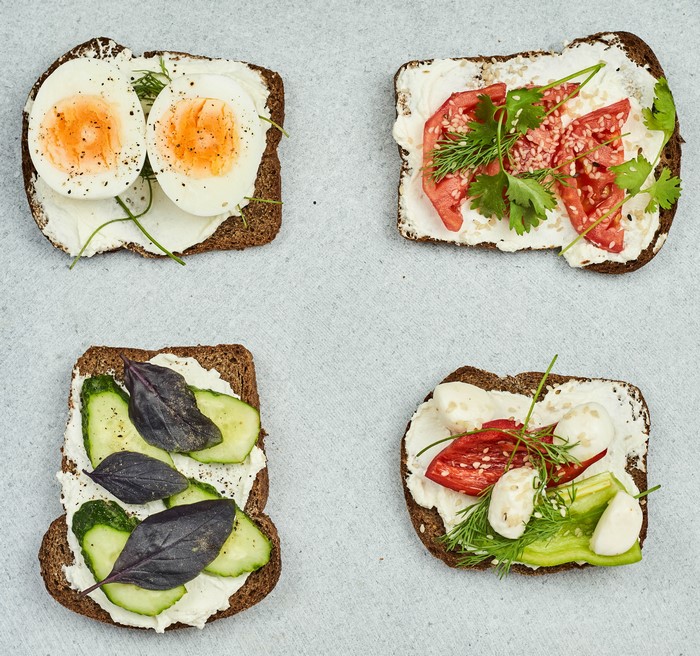 Four open-faced sandwiches with eggs, tomatoes, and cucumbers