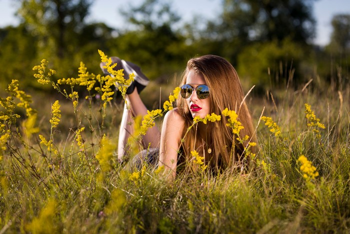 Woman with sunglasses lying in grass with yellow flowers