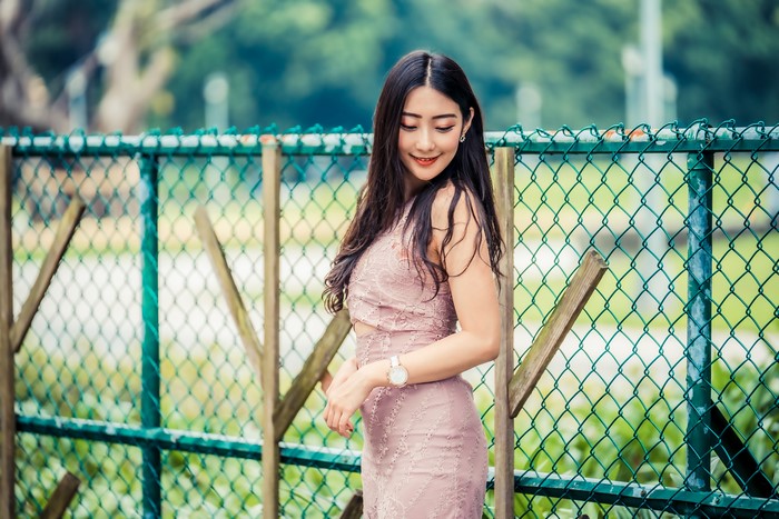 Asian woman in a pink dress by a fence