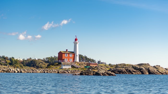 Fisgard Lighthouse on a rocky coast under a blue sky