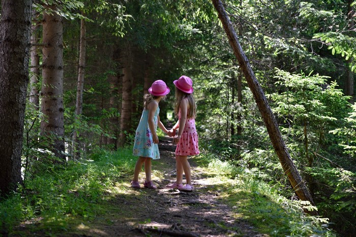 Two little girls in hats holding hands on a forest trail