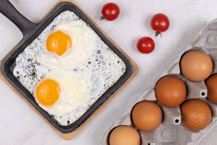Fried eggs in a pan with tomatoes and eggs in a carton