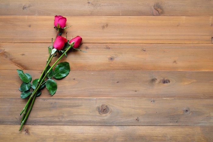 Three red roses on a wooden background