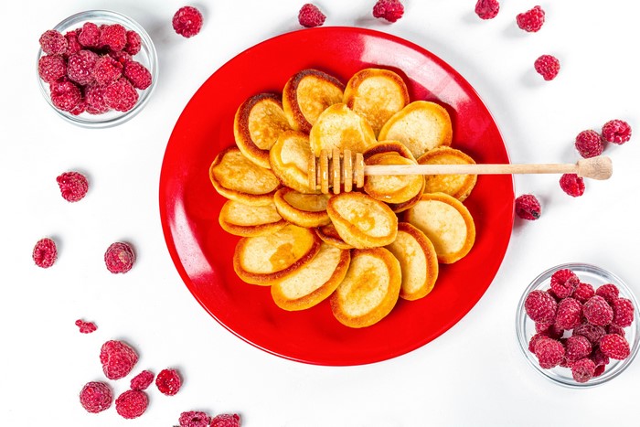 Mini pancakes with raspberries and honey on a red plate