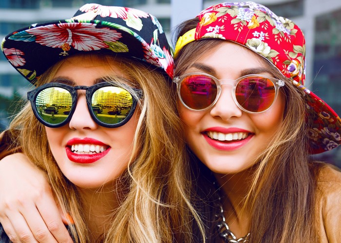 Two young women wearing baseball caps and sunglasses
