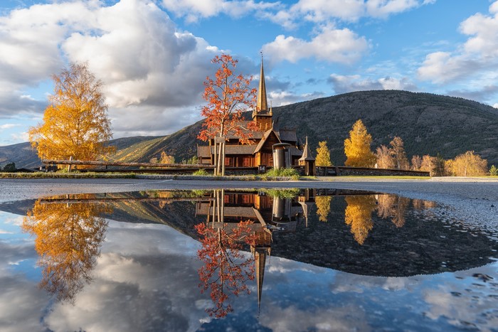 Wooden church in Norway with autumn trees and reflection