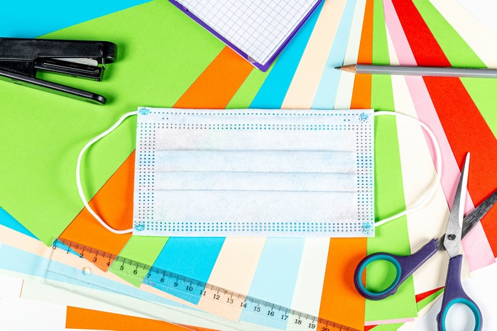 Face mask and school supplies on colorful paper