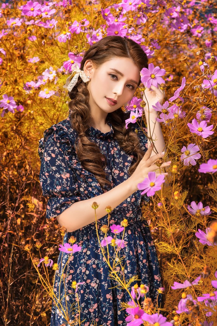 Asian woman with brown hair in a floral dress among cosmos flowers