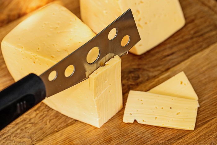 Cheese being cut with a knife on a wooden board