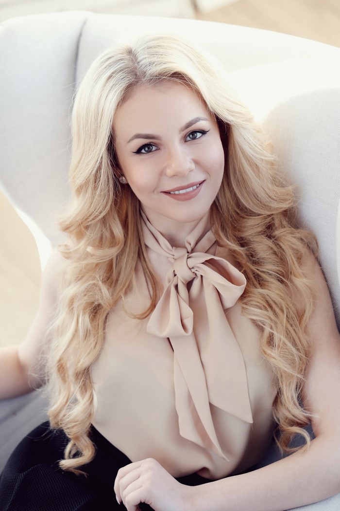 Blonde woman with bow blouse sitting in chair