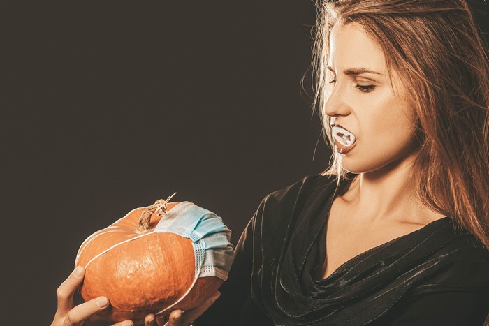 Woman with vampire teeth holding a pumpkin with a mask