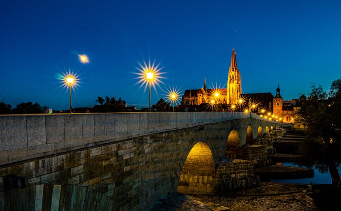 Stone bridge at night with illuminated church in Regensburg, Germany