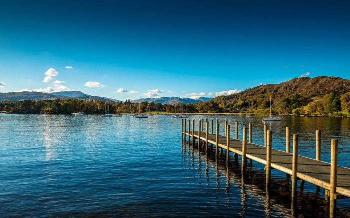Wooden pier on a lake with sailboats and mountains
