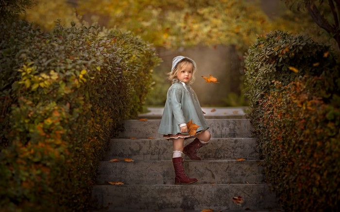 Little girl on autumn stairs with falling leaves