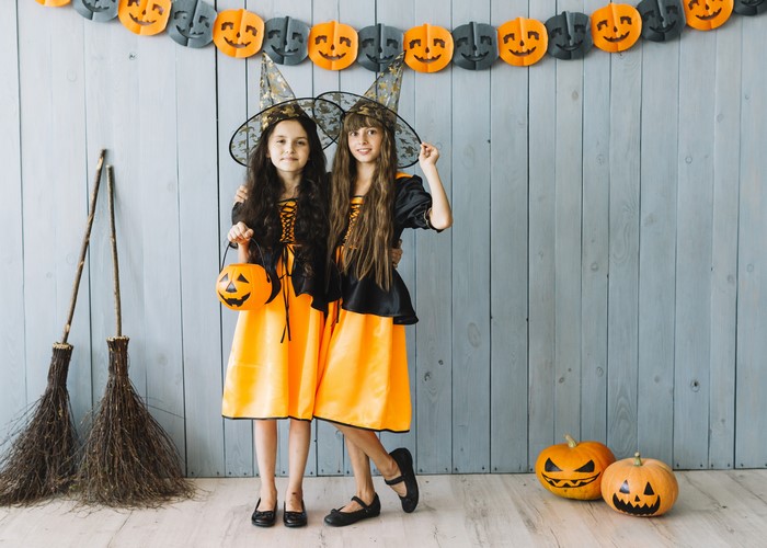 Two little girls in witch costumes with pumpkins