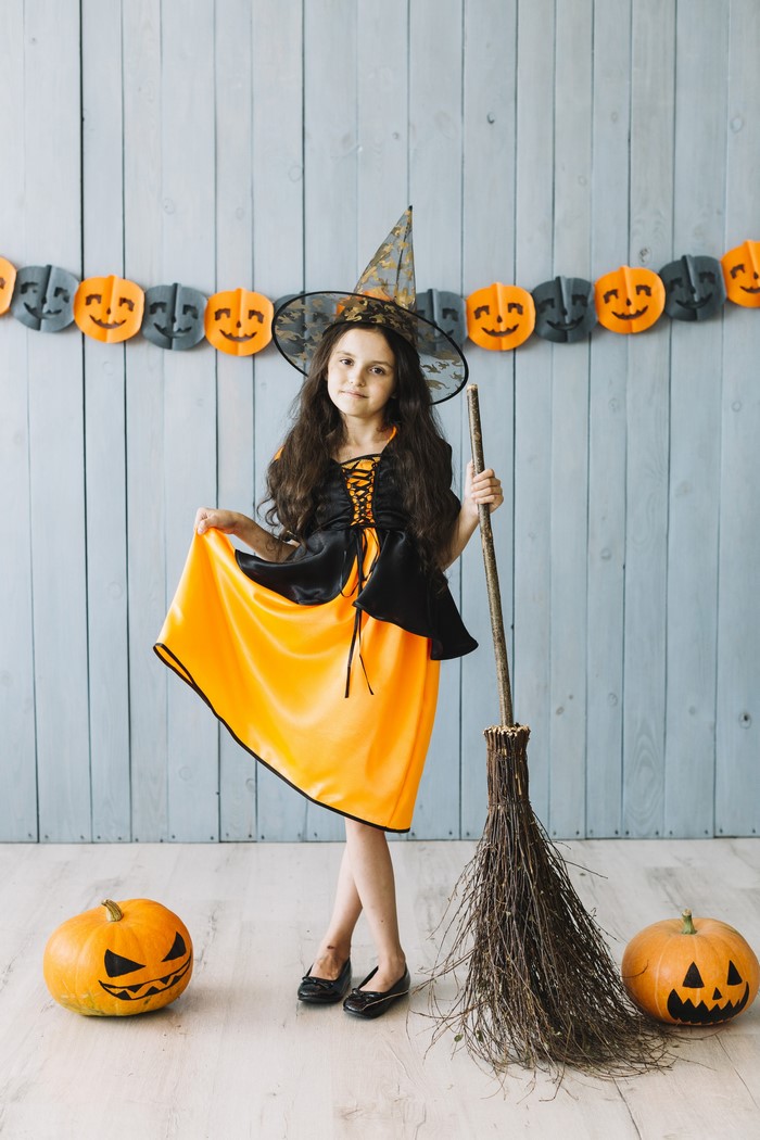 Girl in witch costume with broom and pumpkins
