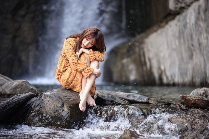 4K Asian Woman Sitting on Stones by Waterfall