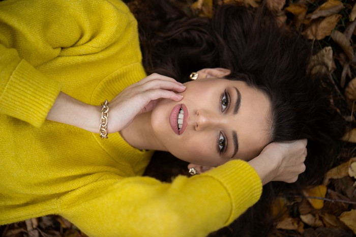 Woman in yellow sweater lying on leaves